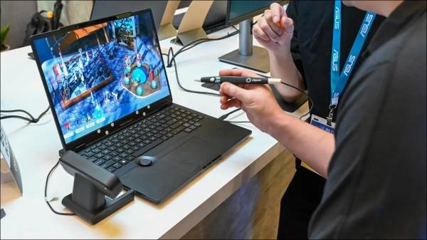 Photo of a laptop with a 3D display, and a hand posed over the keyboard holding a sytuls
