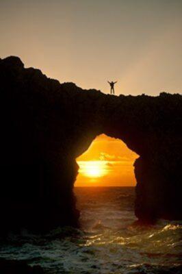 Photo of a rock archway silhouetted with the sun positioned inside the arch