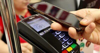Hand holding a smartphone over a point of sale payment terminal