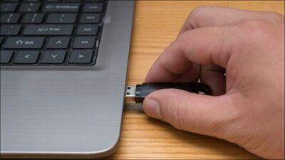 Part of a laptop seen with a hand inserting a USB stick