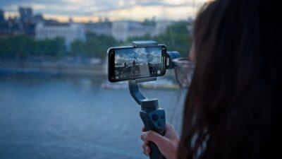 Person with long hair holding a gimbal with a phone mounted on top and showing a camera view on screen