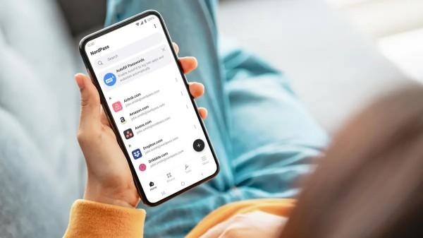 Hand holdinga smartphone. On the screen is the NordPass app listing a few websites.