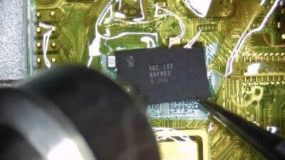 Close view of a motherboard with a chip being lifted, and the nozzle of a heat gun pointed at it.