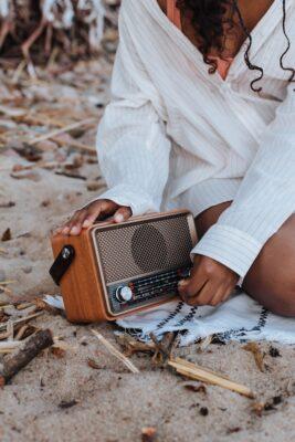 Woman sitting on the sand with a radio, and tuning the knob