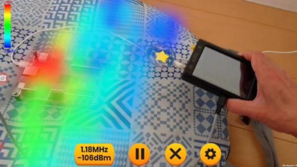 Hand held device being held over a blanket with a computer board, showing different colours above it representing signal strengths being displayed as augmented reality