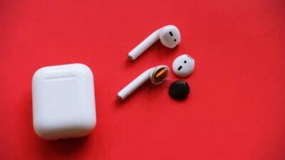 Red background, with white AirPods case, and two AirPods, one of which has its head disassembled.