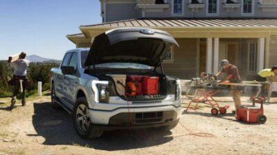 Ford F-150 Lightning with its hood open, and power tools plugged into it via extension cables.