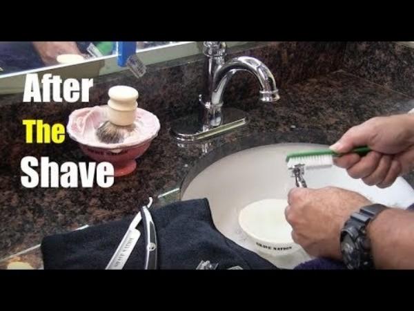 View of a basin with a straight razor being cleaned, and behind basin is a shaving bowl with a shaving brush standing in it