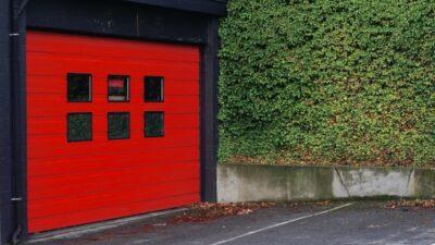 Bright red garage door with a green hedge to the right