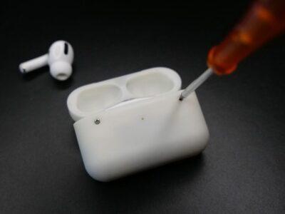 AirPods case showing silver screw heads, one of which has a screwdriver positioned over the screw head.