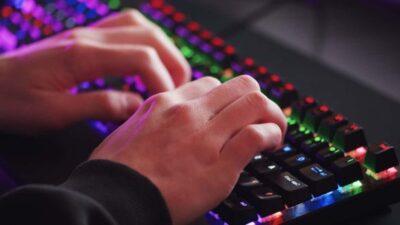 Two hands busy typing on a keyboard with multi-coloured backlighting of the keys