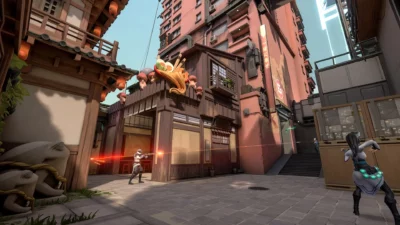 Three gaming characters shooting at each other, with a backdrop of light red buildings with a wooden structure attached to the front of the centre building.
