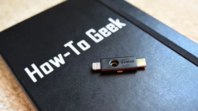 A black journal with the title "How-To-Geek" written on it. On the journal rests a black and gold USB Yubikey with the title Yubico showing on it.