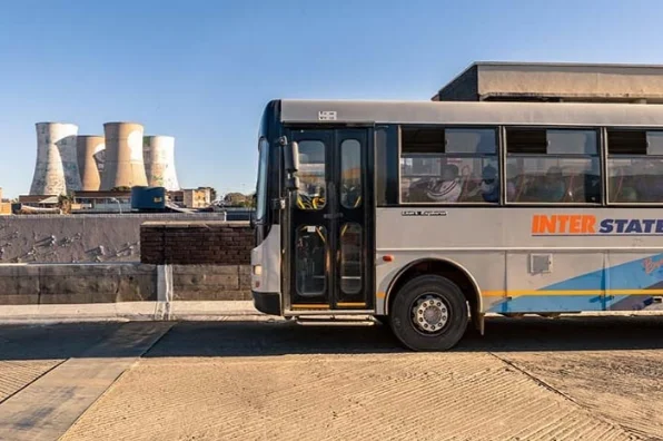 Side view of a bus, with some power station smoke stacks in the background, and clear blue sky