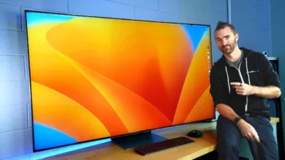 Man sitting next to a very large screen, with his finger pointing at the screen