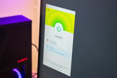 A phone screen showing the ExpressVPN window open with a green connection button in the centre, and underneath that it says Connected, current location USA New York. It says Connected You can use other apps securely.