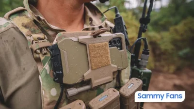 Close view of a soldier's chest, wearing camouflage, with a rugged looking phone strapped to the front of his chest.