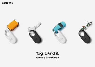 Four smarttag tracker devices with holes for keyrings. Two are white, and two are black. One has a key attached to it, another has a miniature suitcase attached, another a miniature blue car, and the last one has a miniature green bicycle attached.