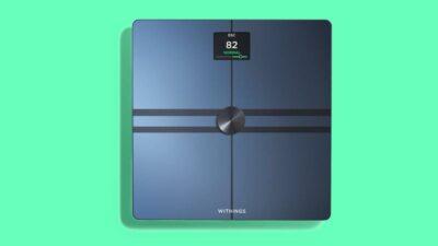 Greean background with top view of a matte black smart scale with a display showing 82 Normal.