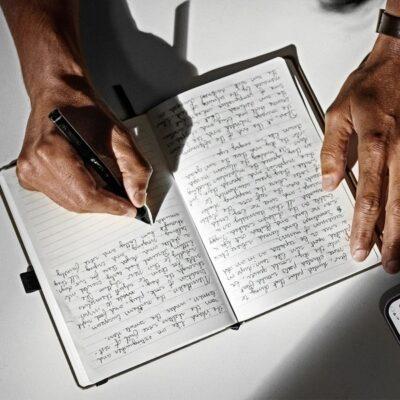 A hand that is writing with a ballpoint pen on a journal page.
