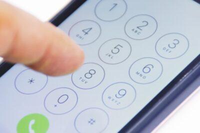 Close view of a smartphone dial pad on screen, with an index finger hovering over the number 8