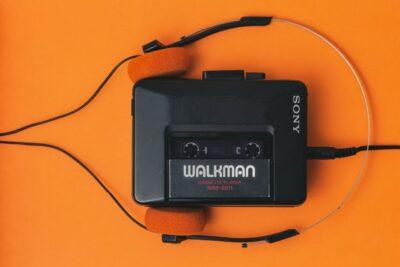 Sony Walkman cassette player on an orange background, with its headphones clipped around the player like a person's head