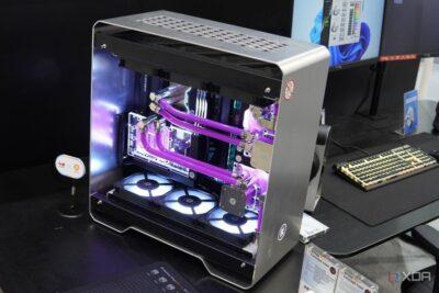 A personal computer box with one side open, exposing the motherboard with two pairs of purple coloured cooling tubes, and three spinning fans at the bottom of the case.