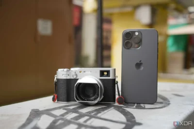 Retro style compact camera facing the viewer, and next to is the rear side of an iPhone showing its 3 lenses