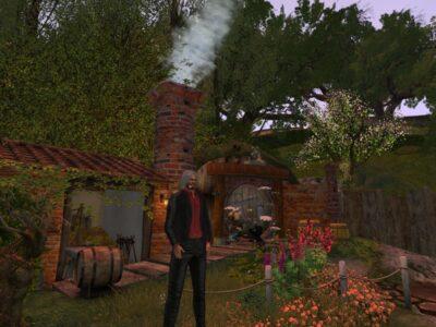 Avatar dressed in a black jacket and pants, with a dark red shirt. He has long grey hair and is smoking a pipe. Behind him is a hobbit like scene with lots of green trees and red brick home with white smoke emitted from the chimney. In front of the house a blacksmith is working at a fire. In the foreground are lots of colourful bushes and flowers.