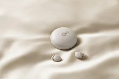 A cream coloured material, with a round white coloured case on top. In front of it are two white coloured earbuds.