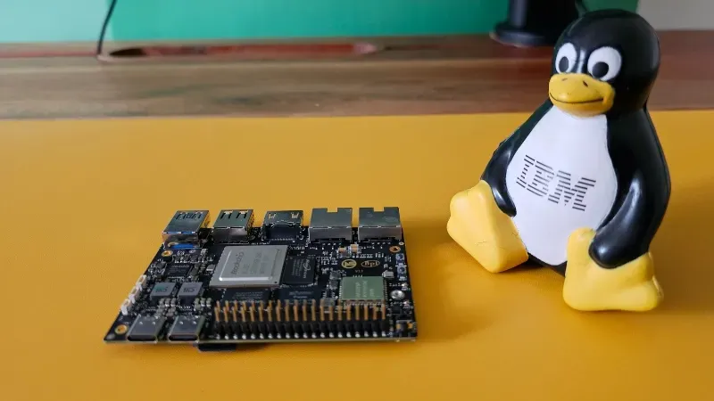 Yellow background with a Raspberberry Pi board resting on it. To the right next to it is a Linux Tux penguin with IBM printed on its front.