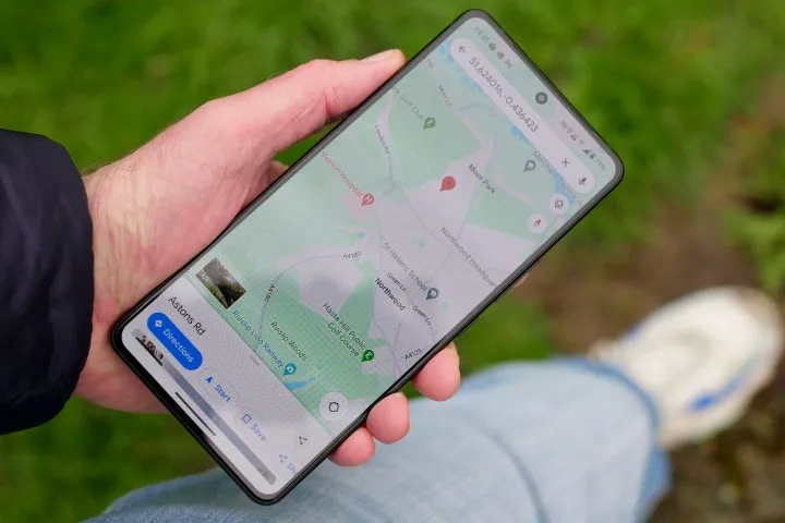 A hand holding a smartphone. On the screen is a typical map and at the bottom of the screen it says Astons Rd with a dark blue icon that says Directions.