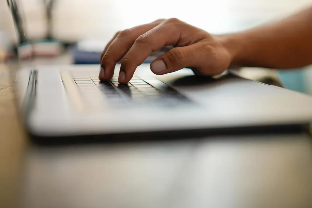 Side view of a laptop keyboard, with a hand hovering over the keyboard.