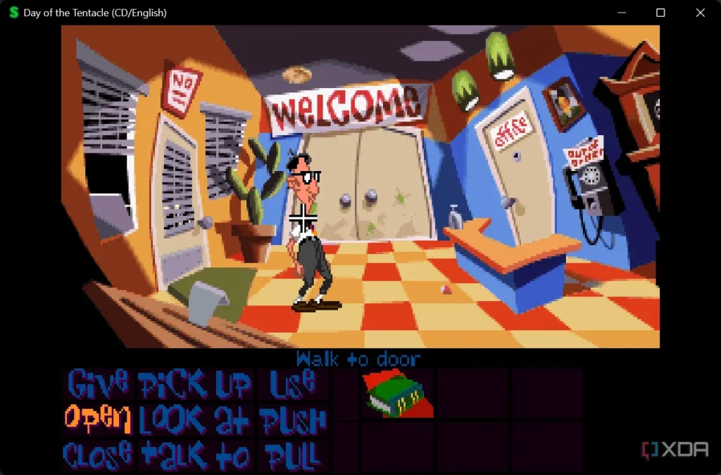 Retro style game from late 1980's or early 1990's with a male cartoon character standing in an office reception area. Signs on walls say Office, Welcome, and on the phone it says out of order. Below the image are options saying Give, Pick Up, Use, Open, Loo At, Push, Close, Talk To, and Pull.