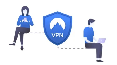 Blue shield logo with letters VPN on it. To the right sits a man with a laptop open on his lap, and to the left sits a woman holding a smartphone.