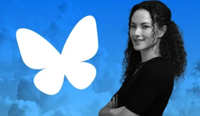 Blue sky background with the white outline of a butterfly. To the right is a woman standing with her arms folded, and smiling at the camera.