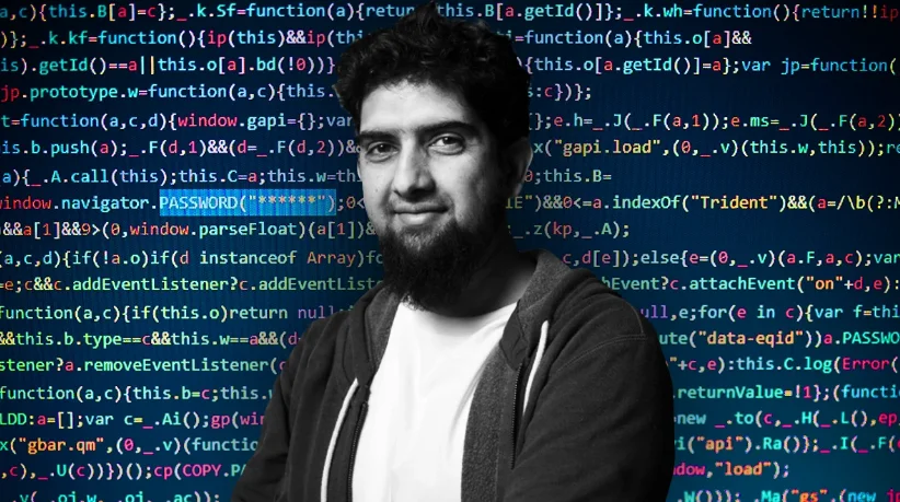 Man smiling at camera with dark hair and a beard. Behind him is a terminal screen covered in lots of different source code with many words highlighted in different colours. The words PASSWORD("******") is highlighted.