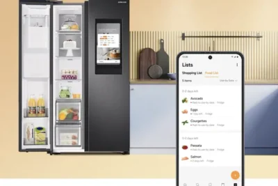 A large double-door fridge, with it's left door standing open. The shelves show a cake, some juice bottles, etc. In the foreground is a smartphone showing an app with the title lists, and under it Shopping List. Items are listed such as avocado, eggs, Salmon, etc.