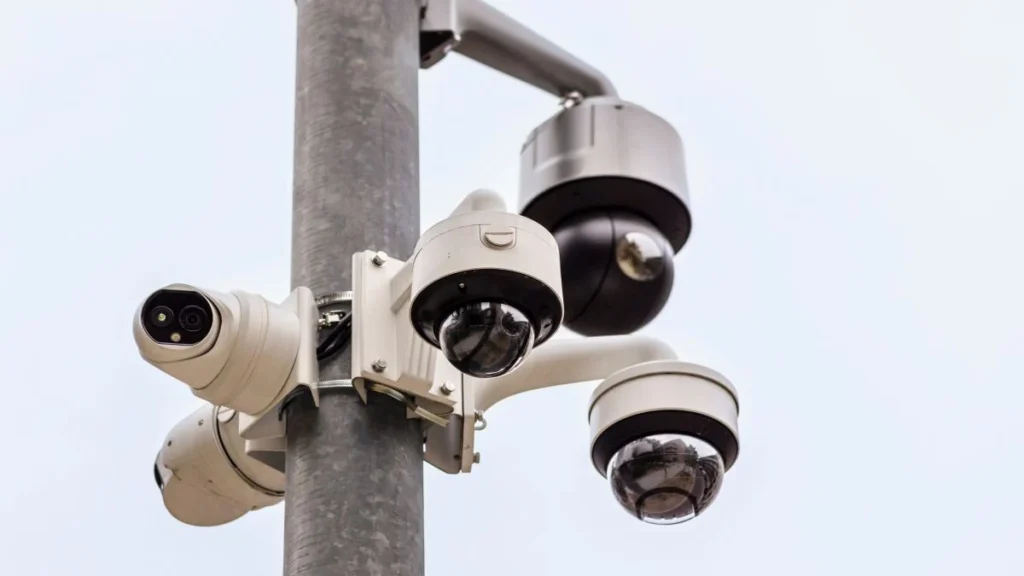 Close view of part of a metal pole. Attached to it are 5 CCTV cameras all pointing in different directions.