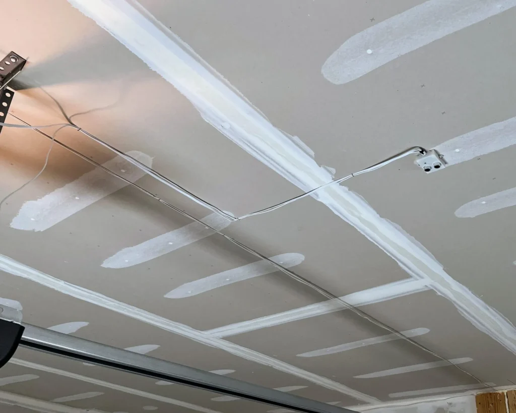 View of the inside ceiling of a garage, showing a small box with two circular sensors mounted on the ceiling above where the car would be. Below that can be seen part of the rail that is used to open the garage door.