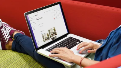 Person sitting with legs crossed and outstretched, with a laptop resting on their legs. On the screen can be seen some images with the title at the top Oct 2024. To the right is a month calendar.