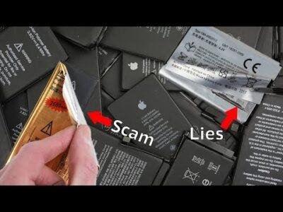 The image shows a pile of counterfeit iPhone batteries in the foreground, with more batteries visible in the background. A person's hand is peeling back the label of one battery to reveal inconsistencies. The most striking detail is the discrepancy between the labeling on the batteries. While some batteries have labels claiming to be authentic Apple products, a close examination reveals inconsistencies and inaccuracies in the labeling.