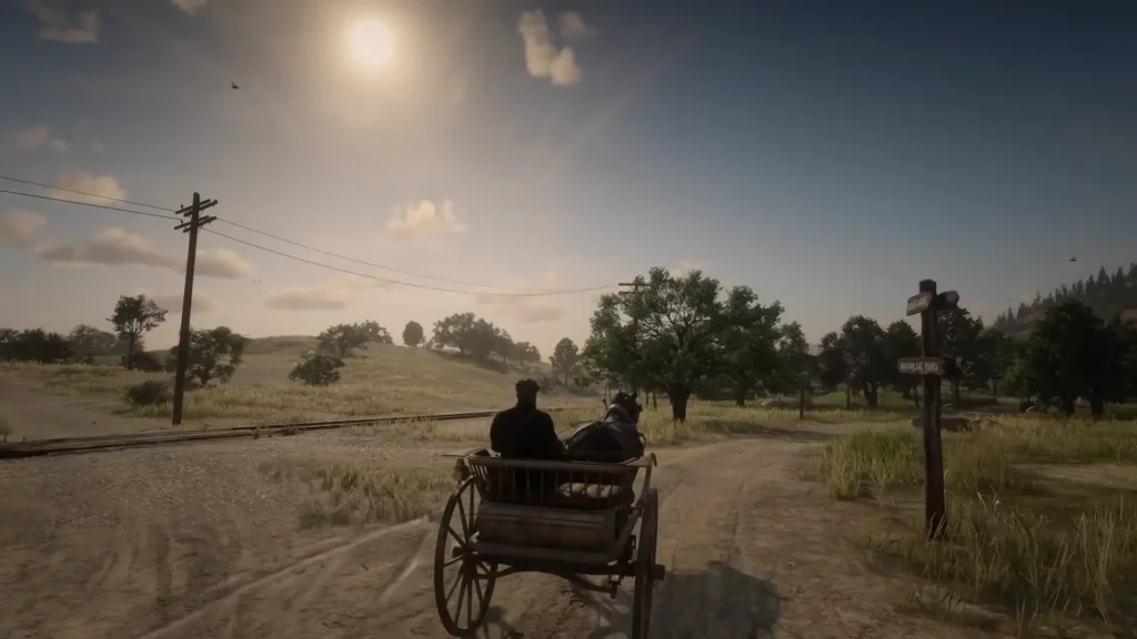 The image shows a person in a horse-drawn cart traveling down a dirt road. In the foreground is the cart itself, appearing to be made of wood with large wooden wheels. The road is dusty and shows tire tracks from previous vehicles. In the background, there's a railway track running parallel to the road, suggesting a rural or countryside setting. Beyond the tracks are sparsely populated trees and rolling hills, with a bright sun dominating the sky. A wooden signpost indicating directions to different locations is also visible in the distance, as well as some birds flying in the upper right corner.