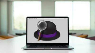 Laptop on a desk displaying a graphic of a magnifying glass over a black hat with a purple band.