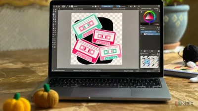 Laptop displaying digital art of colorful cassette tapes on a wooden table with small pumpkins nearby.