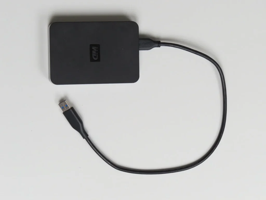 A black external hard drive with a USB cable attached, resting on a white surface.