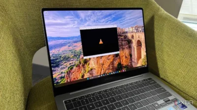 A laptop displaying a scenic landscape wallpaper with a VLC media player opened in the foreground, set against a green upholstery backdrop.