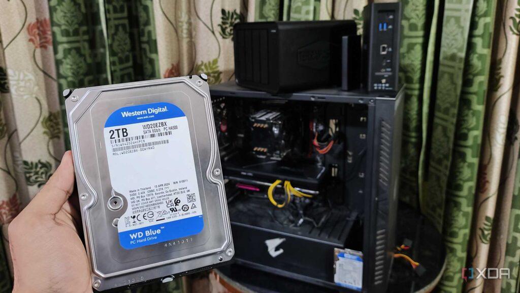 A person holds a 2TB Western Digital hard drive in front of a computer case with visible internal components and cables.