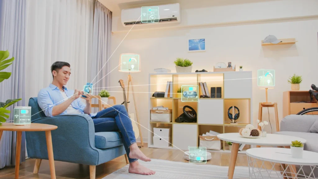 A person seated in a cosy living room interacts with smart home devices, showcasing modern technology and a relaxed atmosphere. There are connecting lines going out from the person's smartphone to the various devices, indicating their phone is connected to the devices.