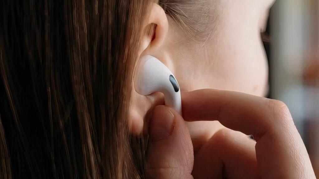 A close-up of a person inserting a wireless earbud into their ear, with long hair partially covering the ear.